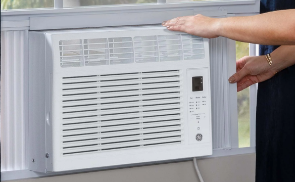 BTU 115V window air conditioner front view, white body with visible front grille and digital display, mounted in window